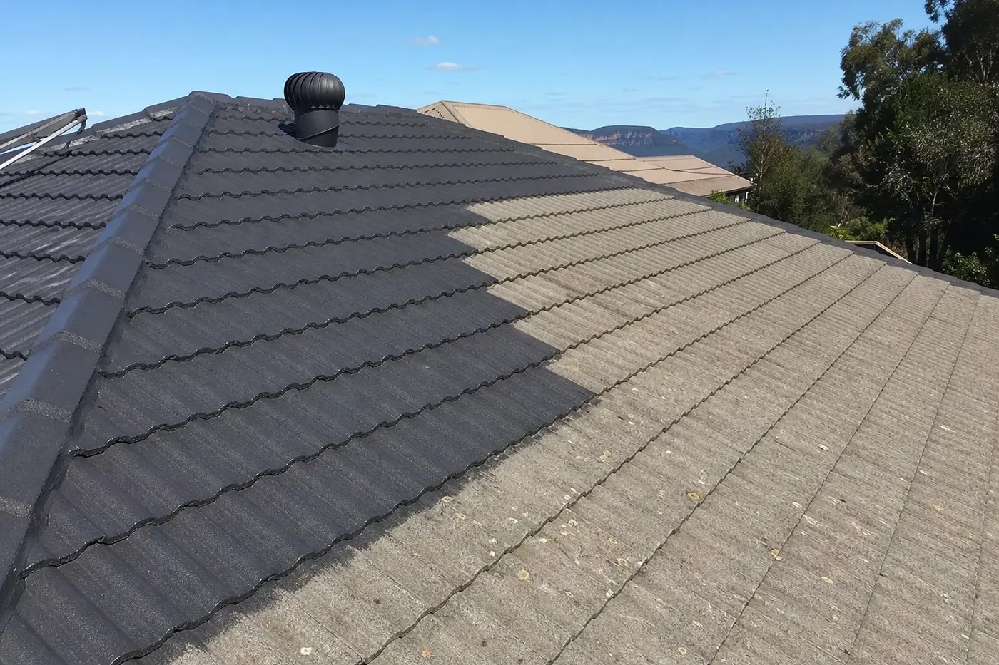 Blue Mountains tile roof mid-repaint, one section freshly coated in charcoal and the rest faded and chalky