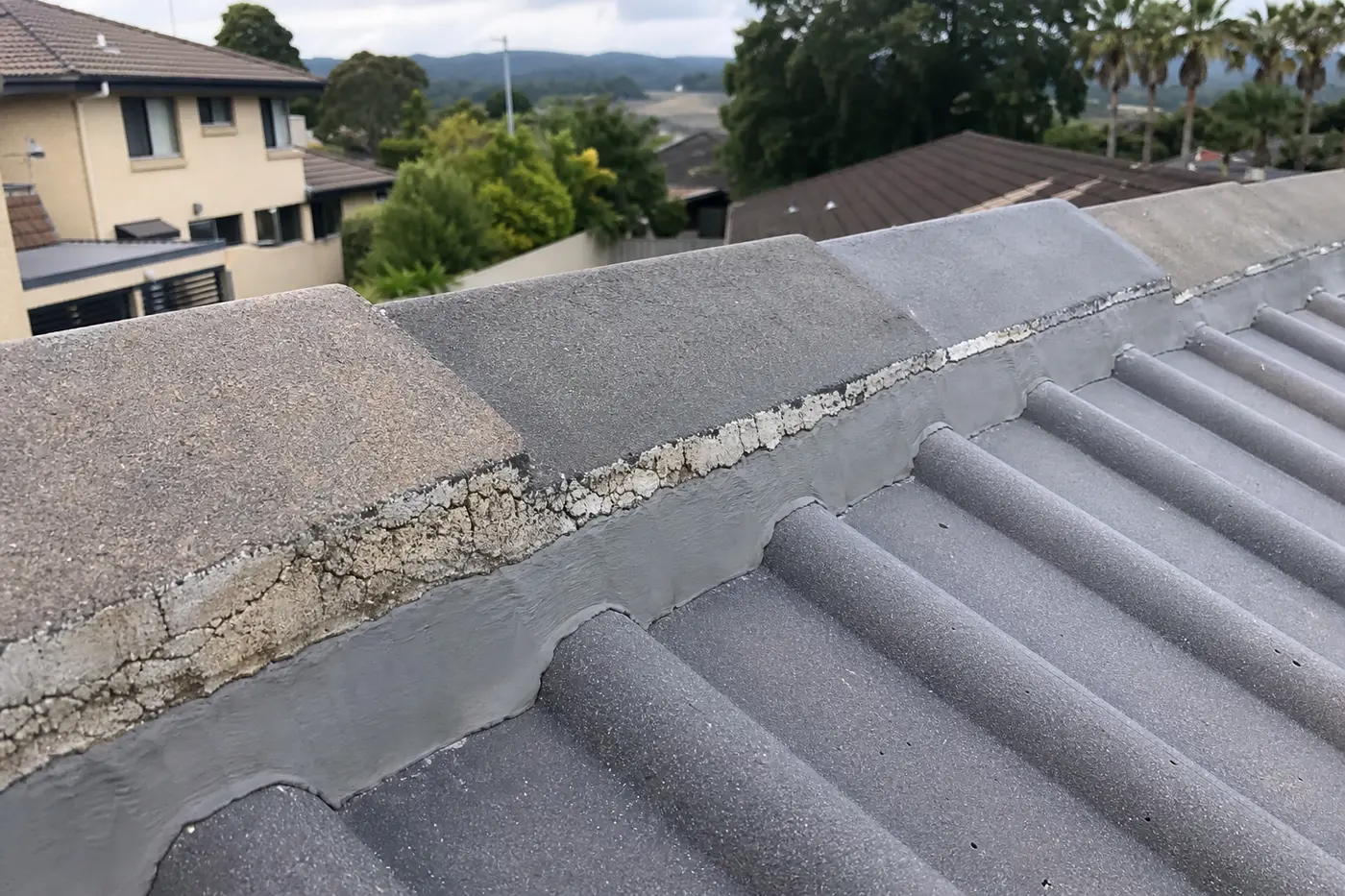 Cracked cement mortar along a tiled roof ridge line next to freshly repointed ridge capping on a Blue Mountains home
