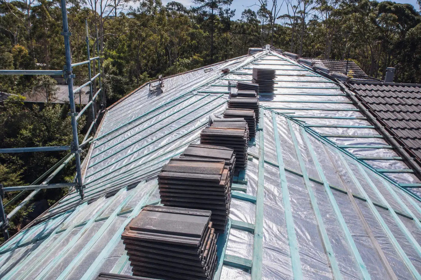 Reflective sarking membrane laid across the rafters of a partly re-roofed Blue Mountains home, tiles stacked ready to go back on
