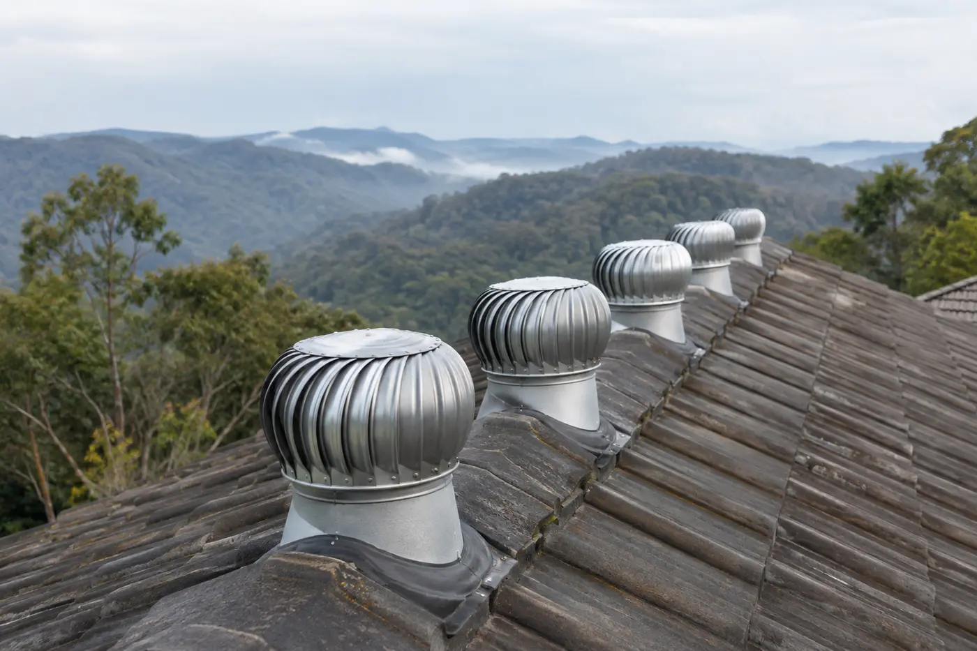 Whirlybird vents along the ridge of a tile roof with misty Blue Mountains bushland behind