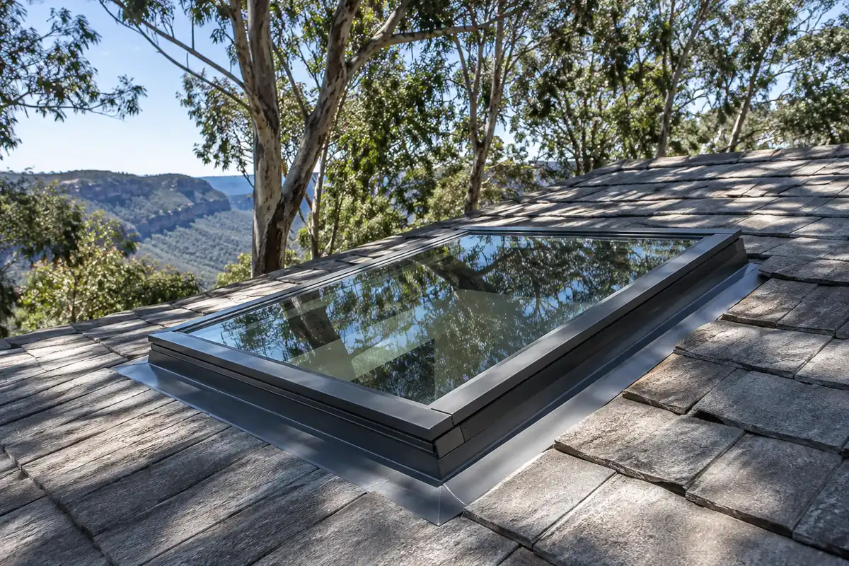 A fixed glass skylight with new metal flashing set into a concrete tile roof under tall eucalypts